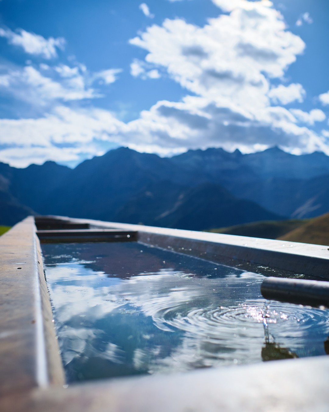 Clouds reflected in a drinking trough in front of the mountains.
