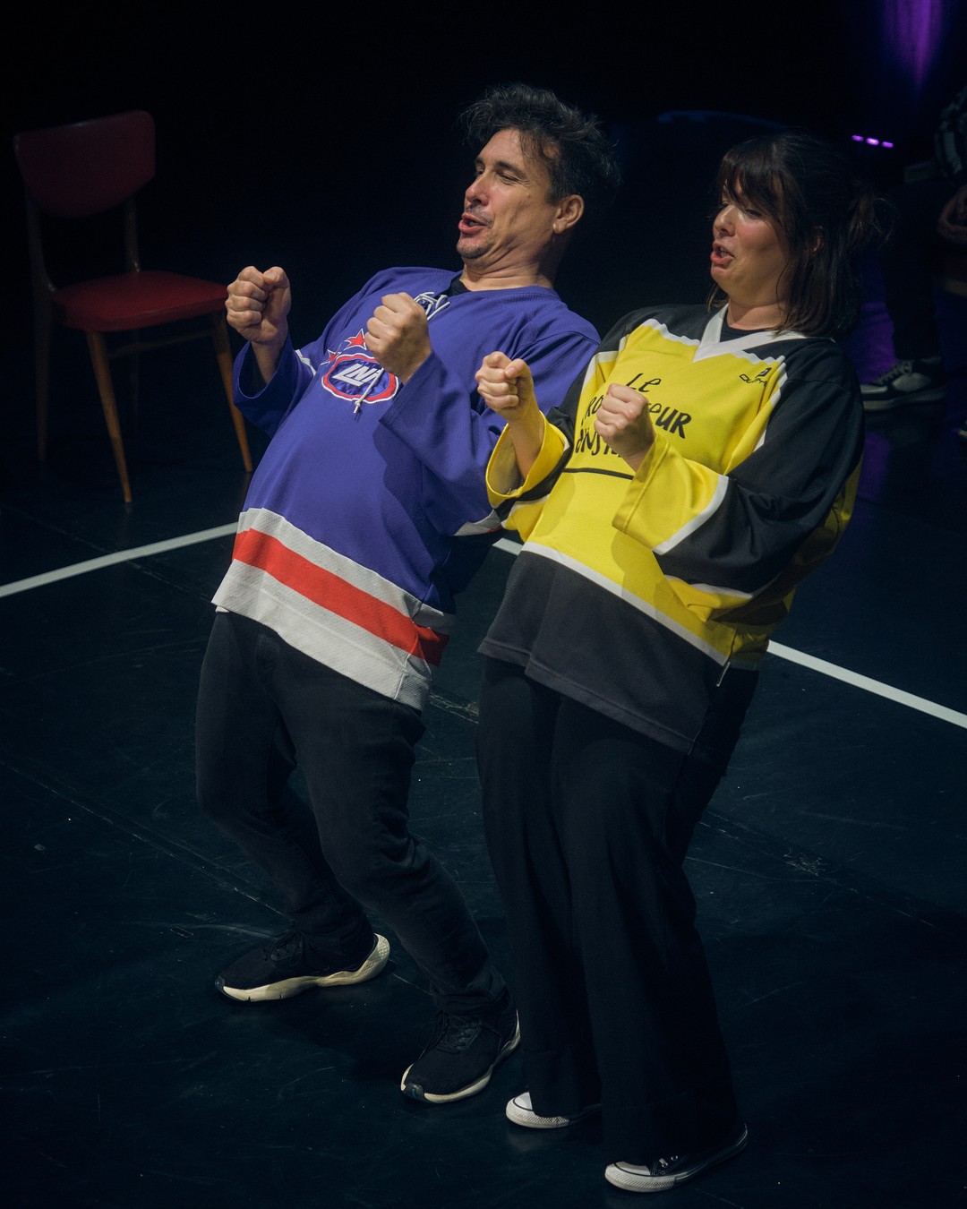 Dos actores interpretan una escena en movimiento bajo luces violetas.